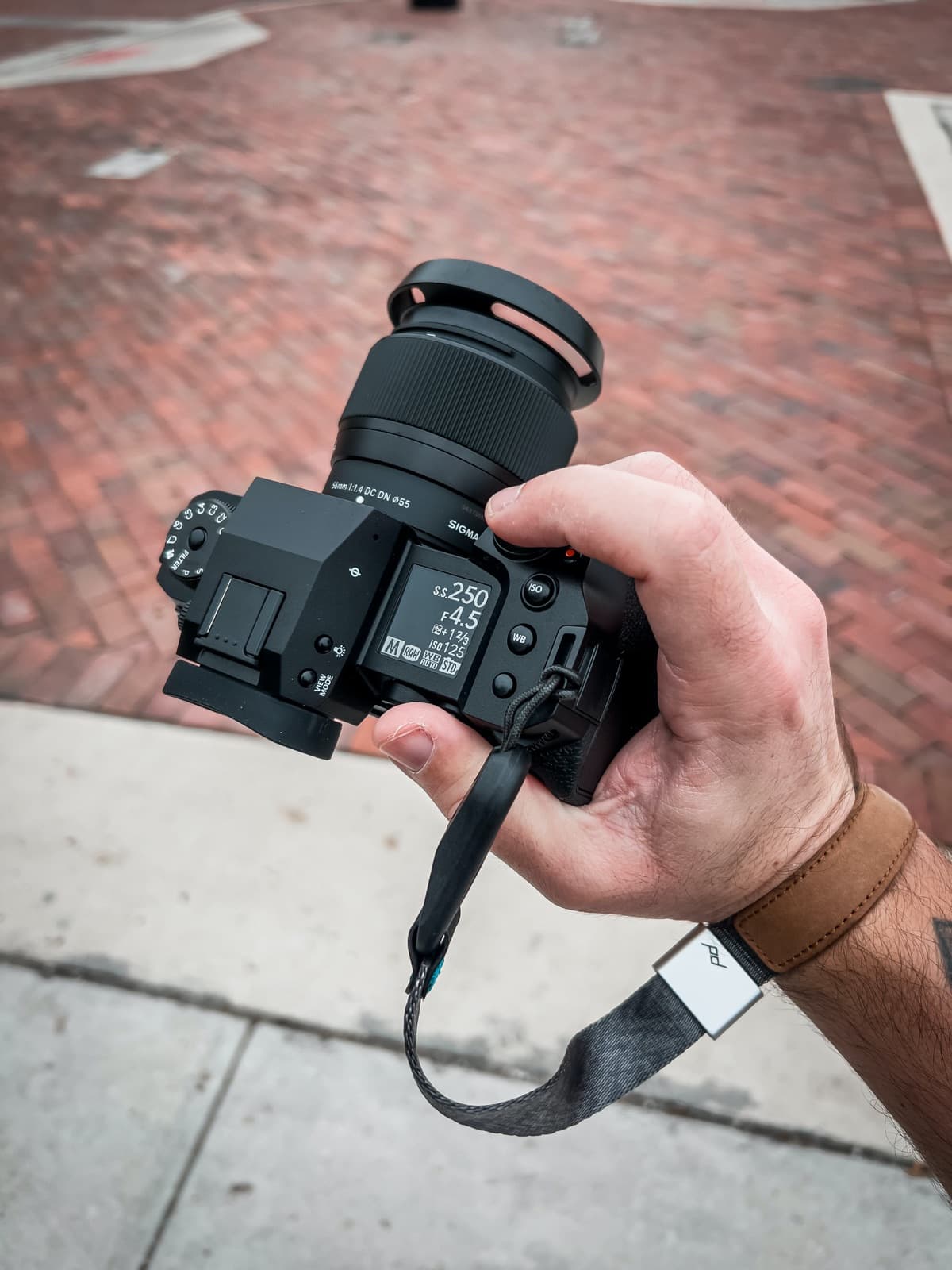 A hand holding a mirrorless camera with shutter speed and aperture showing on its rear screen